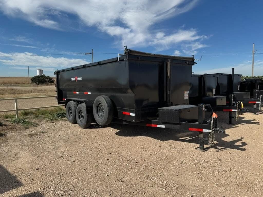 Black dump trailer with its bed raised on a gravel lot