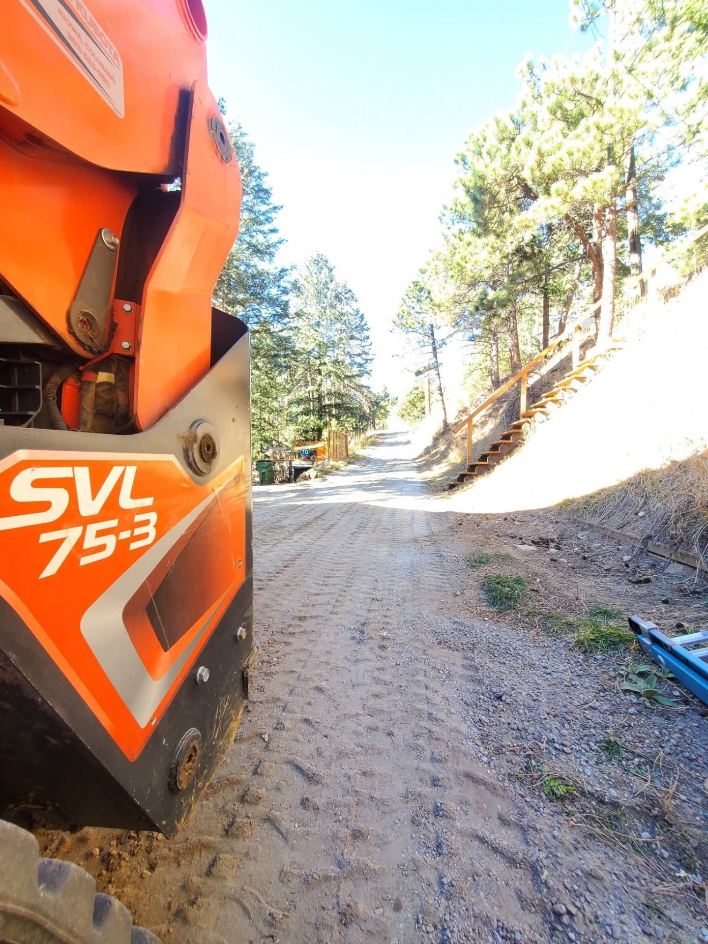 Close-up of a skid steer cab with work gloves resting on the machine, backlit at sunset